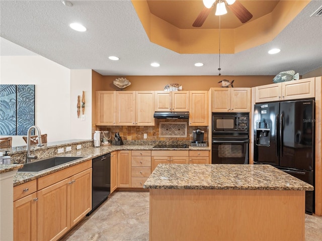 kitchen with a raised ceiling, under cabinet range hood, light brown cabinetry, black appliances, and a sink