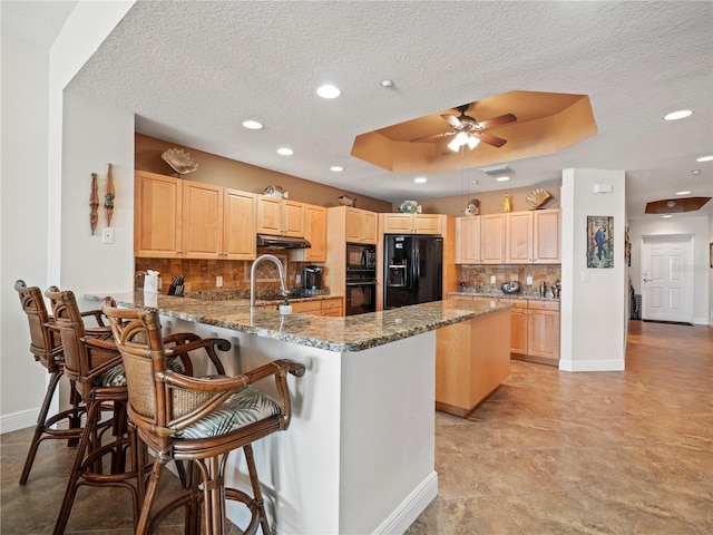 kitchen with a breakfast bar area, a peninsula, black appliances, and light brown cabinetry