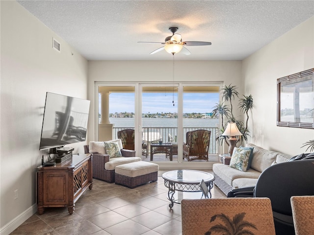 living area with baseboards, visible vents, a ceiling fan, tile patterned flooring, and a textured ceiling