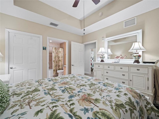 bedroom with a raised ceiling, connected bathroom, and visible vents