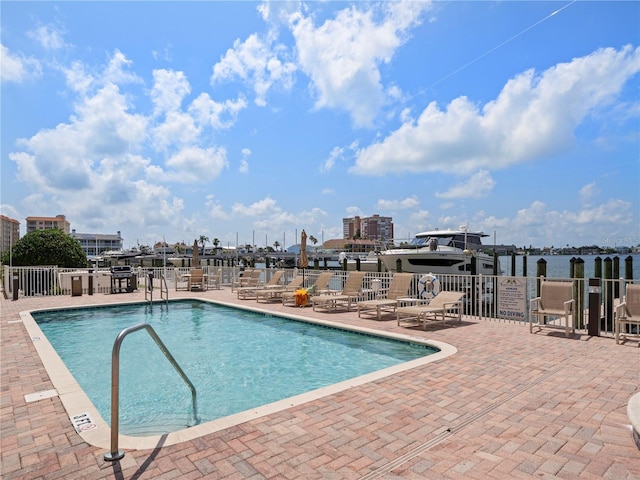 pool featuring a water view, a patio area, and fence