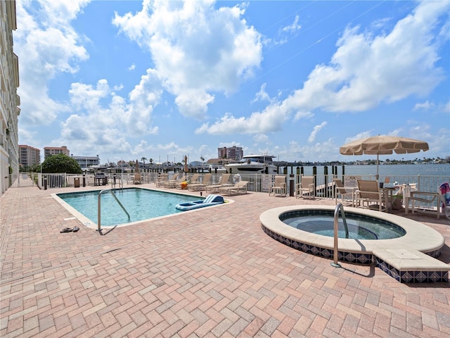 community pool featuring a water view, a hot tub, fence, and a patio