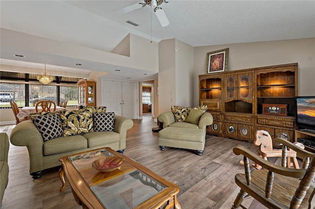 living room featuring a textured ceiling, high vaulted ceiling, wood finished floors, visible vents, and a ceiling fan