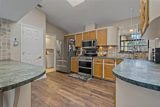 kitchen with decorative light fixtures, dark countertops, washer / clothes dryer, appliances with stainless steel finishes, and a sink