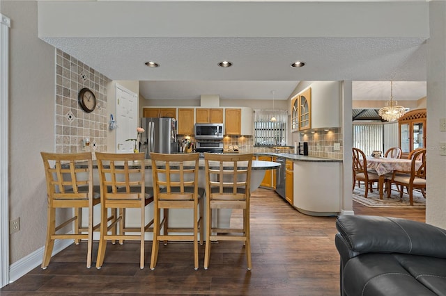 kitchen with pendant lighting, stainless steel appliances, wood finished floors, glass insert cabinets, and an inviting chandelier