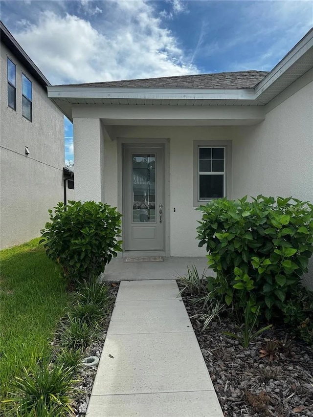 entrance to property featuring a shingled roof and stucco siding