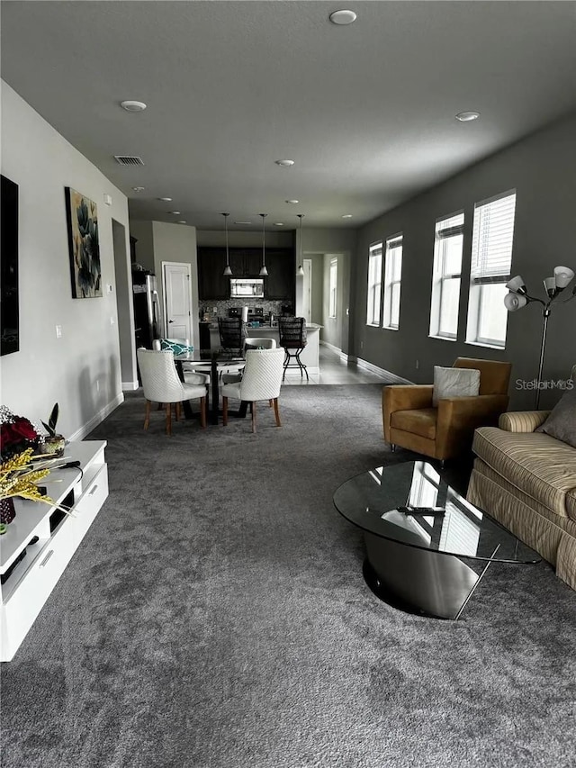 living room with dark carpet, visible vents, and baseboards