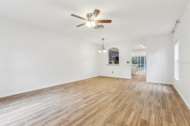 unfurnished living room featuring arched walkways, visible vents, light wood-type flooring, baseboards, and ceiling fan with notable chandelier