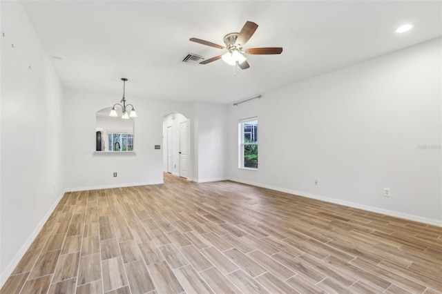 unfurnished living room with arched walkways, light wood finished floors, ceiling fan with notable chandelier, and visible vents