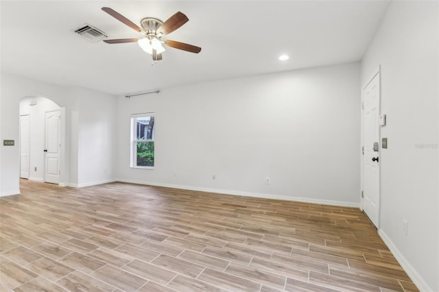 spare room with light wood finished floors, baseboards, visible vents, arched walkways, and a ceiling fan