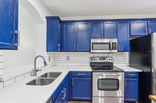 kitchen featuring light stone counters, blue cabinetry, stainless steel appliances, tasteful backsplash, and a sink