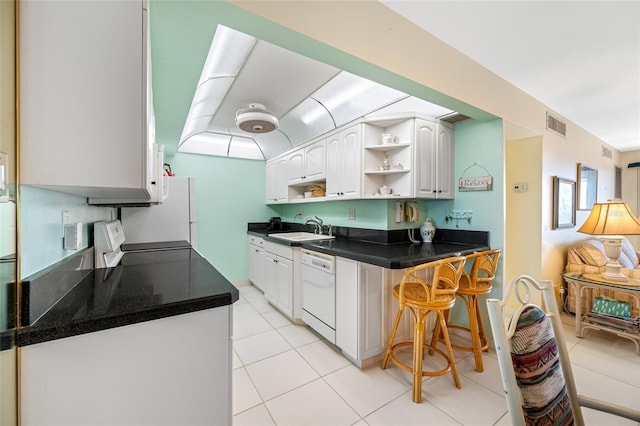 kitchen with white cabinets, a breakfast bar area, white dishwasher, open shelves, and a sink