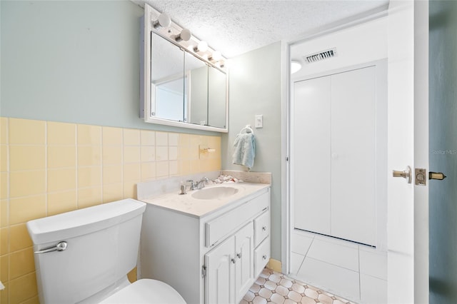 bathroom featuring tile walls, visible vents, toilet, a textured ceiling, and vanity