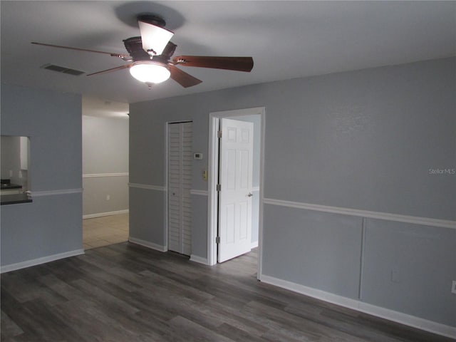 unfurnished room with ceiling fan, dark wood-style flooring, visible vents, and baseboards