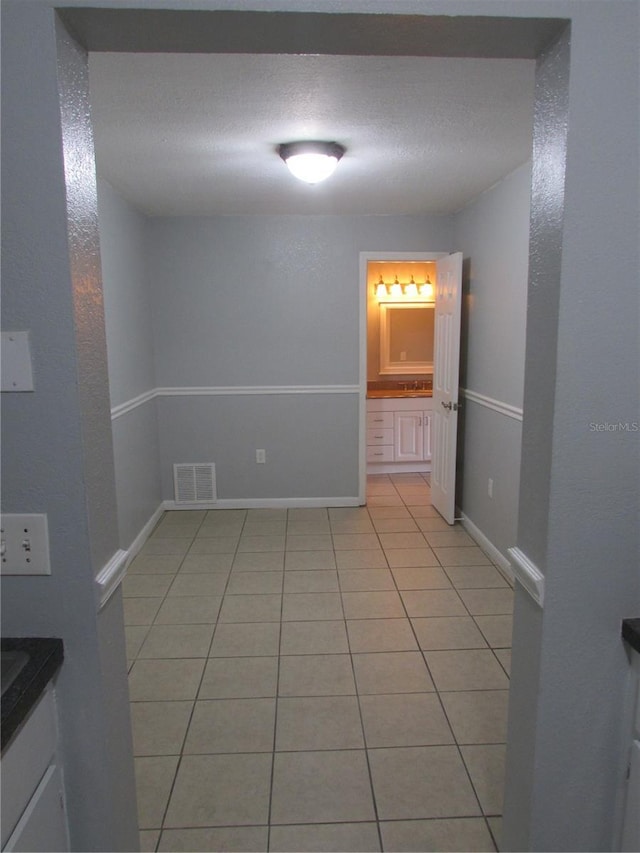 spare room featuring light tile patterned floors, baseboards, visible vents, and a textured ceiling