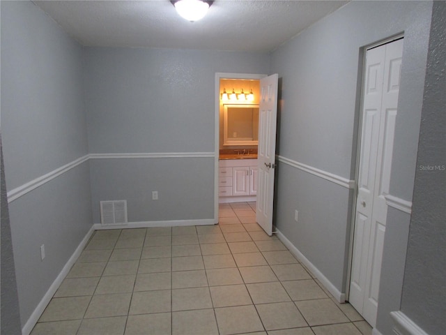 interior space with baseboards, visible vents, a textured ceiling, a sink, and light tile patterned flooring