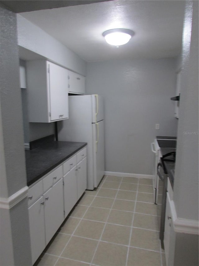 kitchen with light tile patterned floors, dark countertops, stainless steel stove, freestanding refrigerator, and white cabinetry