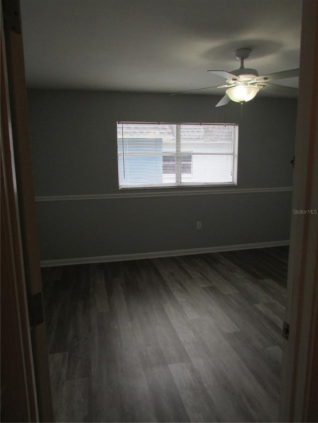 empty room with dark wood-type flooring, baseboards, and a ceiling fan