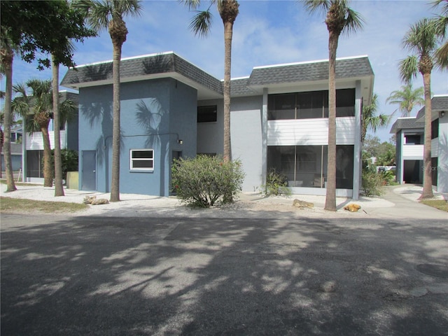 exterior space featuring a shingled roof, stucco siding, and mansard roof