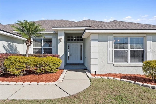 doorway to property featuring a yard, a shingled roof, and stucco siding