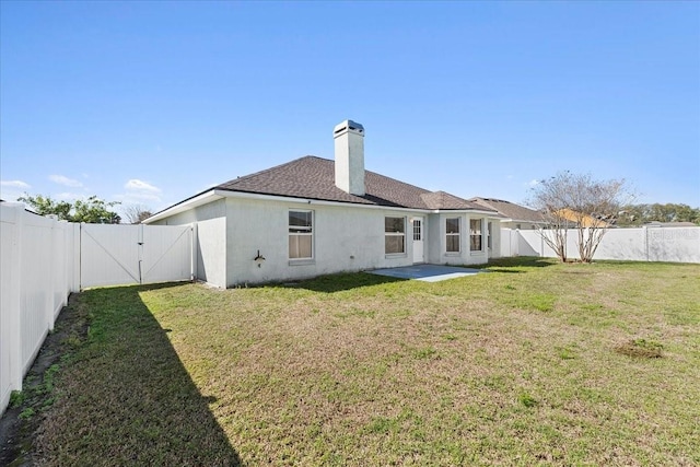 back of house featuring a gate, a fenced backyard, a yard, and a chimney