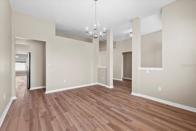 spare room with an inviting chandelier, baseboards, and wood finished floors