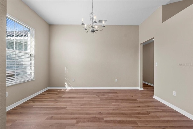 empty room featuring light wood finished floors, an inviting chandelier, and baseboards