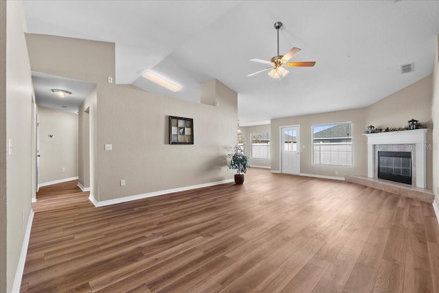 unfurnished living room with visible vents, a ceiling fan, vaulted ceiling, wood finished floors, and a tile fireplace