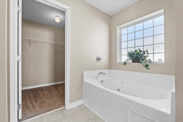 full bathroom featuring a jetted tub, a spacious closet, baseboards, and tile patterned floors