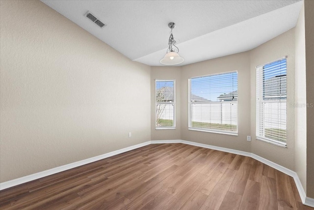 spare room with baseboards, visible vents, and wood finished floors