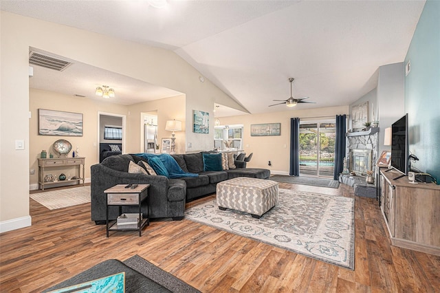 living area featuring dark wood-style floors, a stone fireplace, vaulted ceiling, and visible vents