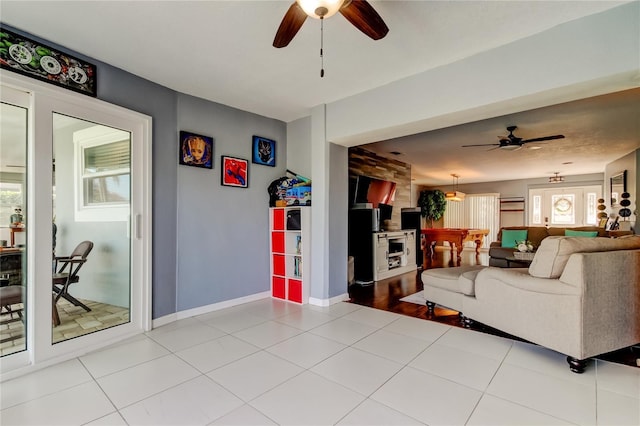 living area featuring a ceiling fan, light tile patterned flooring, and baseboards