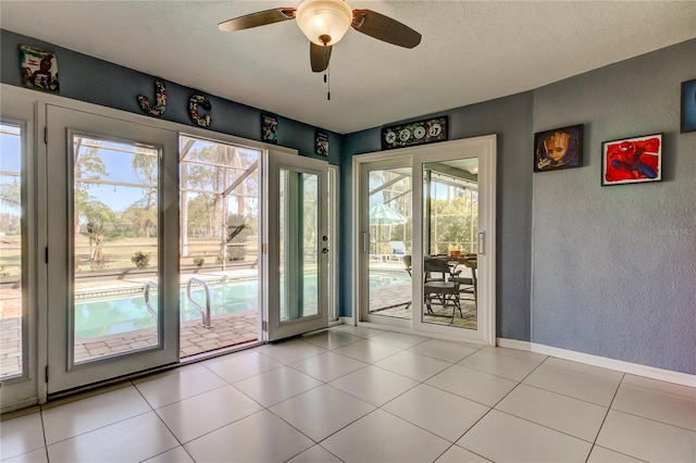 entryway featuring ceiling fan, a textured wall, baseboards, and light tile patterned floors