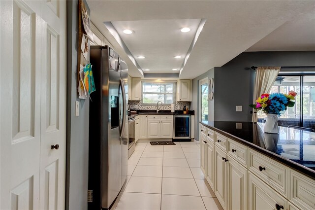 kitchen featuring light tile patterned floors, tasteful backsplash, beverage cooler, appliances with stainless steel finishes, and a sink