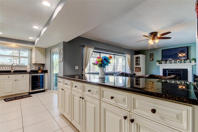 kitchen featuring wine cooler, light tile patterned flooring, a sink, open floor plan, and dark stone counters