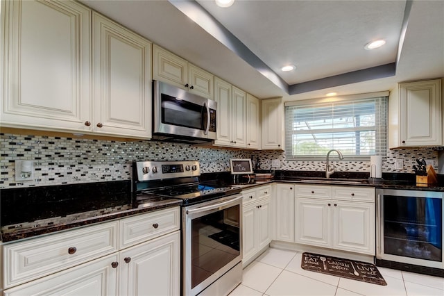 kitchen with wine cooler, stainless steel appliances, a raised ceiling, a sink, and dark stone countertops