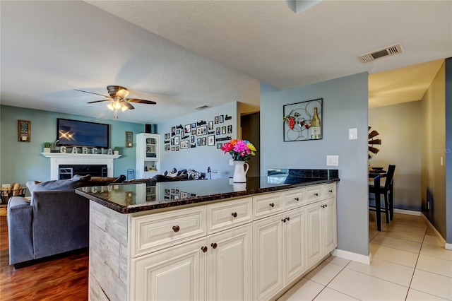 kitchen with visible vents, white cabinets, open floor plan, dark stone countertops, and a fireplace