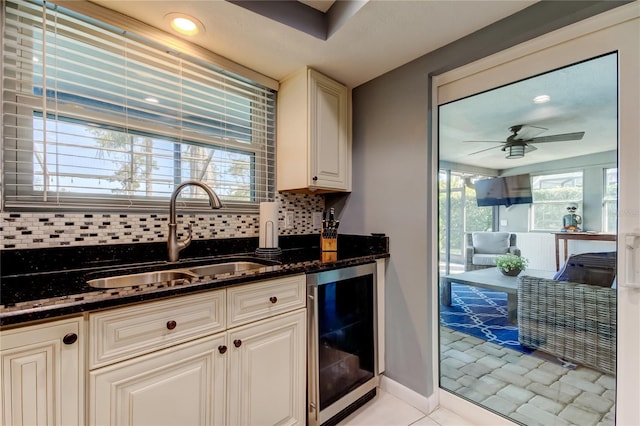 kitchen with beverage cooler, a sink, a ceiling fan, tasteful backsplash, and dark stone countertops