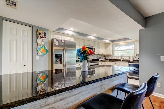 kitchen with a raised ceiling, visible vents, backsplash, appliances with stainless steel finishes, and dark stone counters