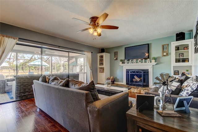 living area featuring dark wood-style floors, ceiling fan, a fireplace with raised hearth, and a textured ceiling