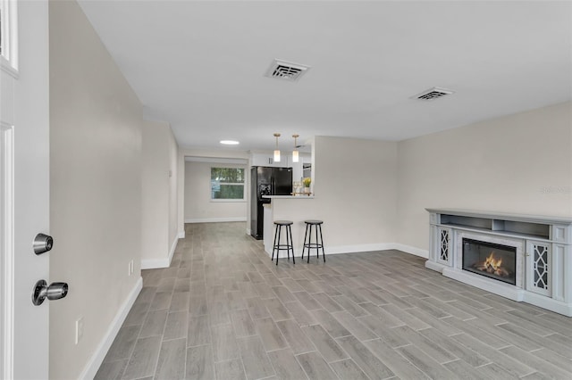 unfurnished living room with a glass covered fireplace, baseboards, visible vents, and light wood finished floors