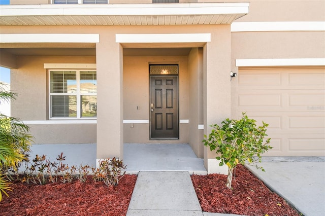 view of exterior entry with an attached garage and stucco siding