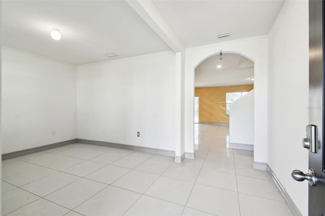 unfurnished room featuring arched walkways, light tile patterned floors, visible vents, wooden walls, and baseboards