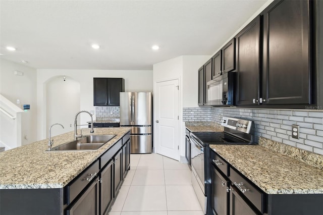 kitchen with light tile patterned flooring, a sink, appliances with stainless steel finishes, backsplash, and an island with sink