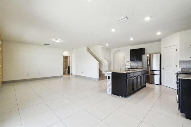 kitchen featuring arched walkways, dark cabinets, a sink, visible vents, and freestanding refrigerator