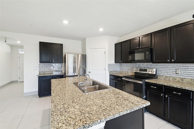 kitchen featuring arched walkways, light tile patterned flooring, stainless steel appliances, a sink, and a center island with sink