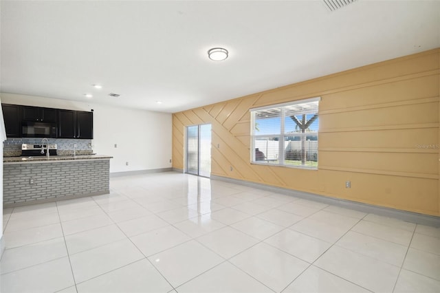 unfurnished living room featuring light tile patterned flooring, wooden walls, a sink, visible vents, and baseboards