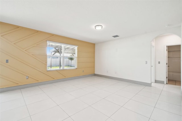 spare room featuring arched walkways, light tile patterned floors, visible vents, and baseboards