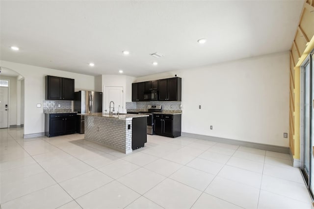 kitchen featuring appliances with stainless steel finishes, arched walkways, decorative backsplash, and light tile patterned floors