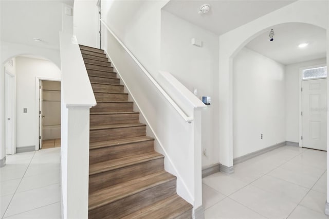 interior space with stairs, arched walkways, baseboards, and light tile patterned floors